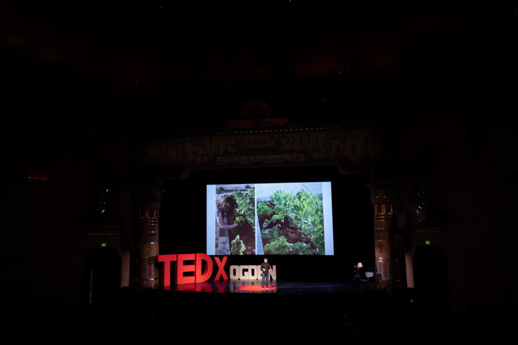 Wide stage view of Zachary Moses TEDxOgden talk with a plants and greenery slide