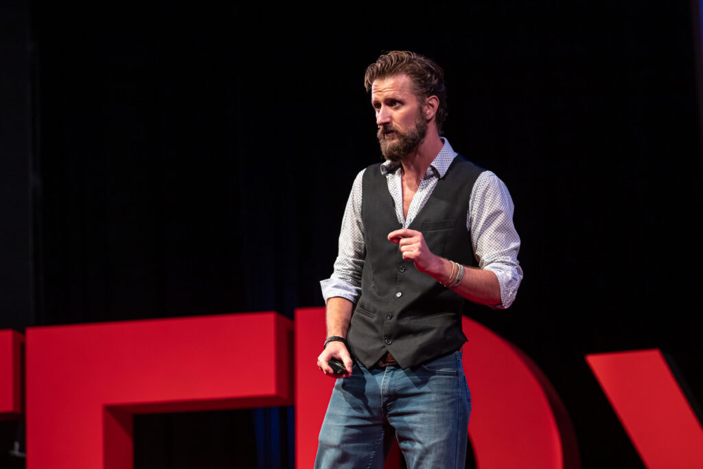 Zachary Moses on the TEDxOgden stage before red TEDx letters