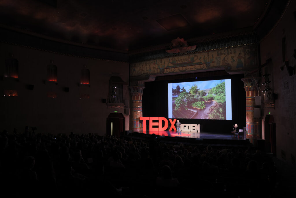 Wide auditorium view of Zachary Moses TEDxOgden talk with a trees and landscape slide
