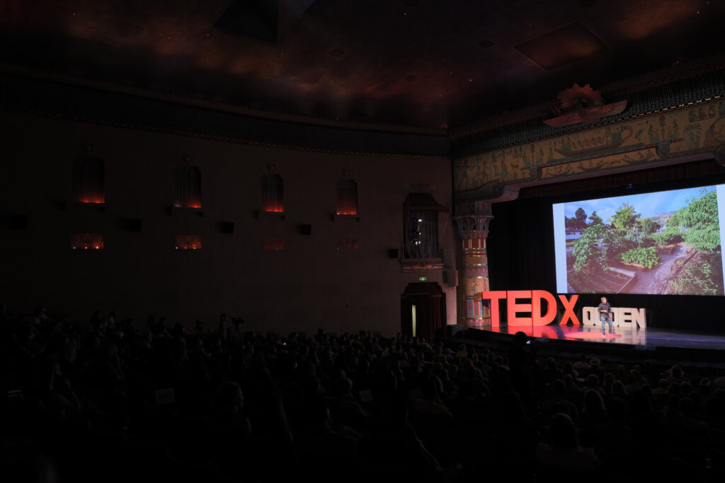 Auditorium view of Zachary Moses TEDxOgden talk with a trees slide behind him
